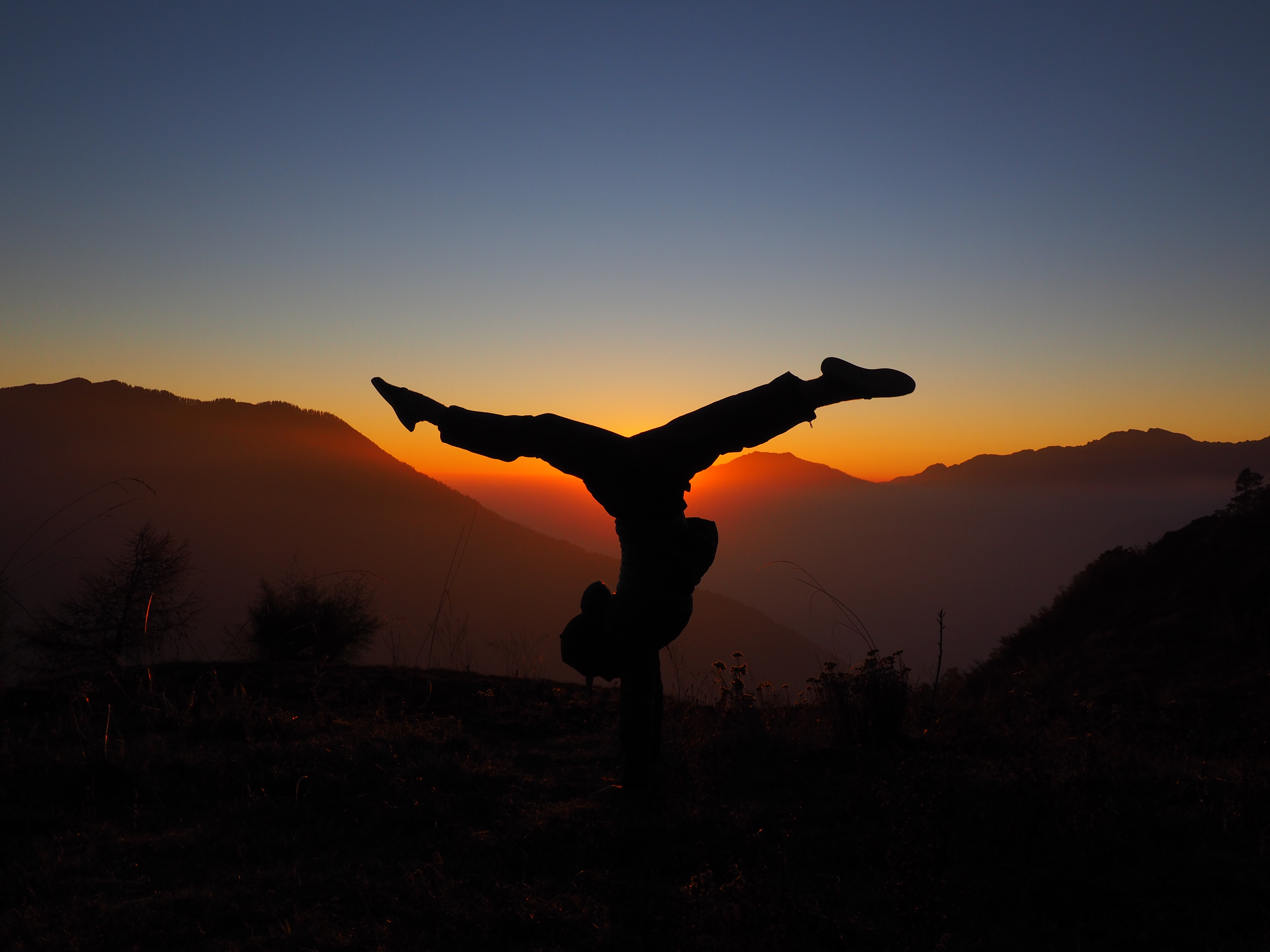 A young women striking a gymanstic pose that blocks out
                    out the sun while on a trek